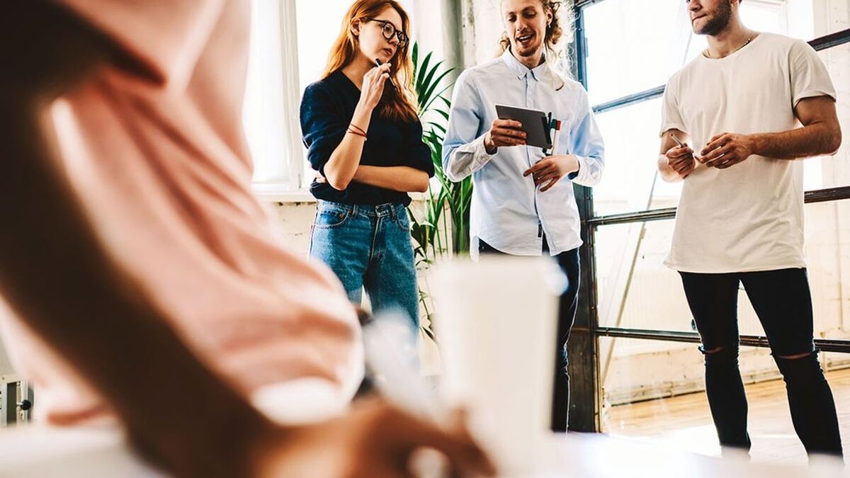 Skilled team of coworkers using application on portable pc for searching information during brainstorming session, male and female students reading news from website via digital tablet on break